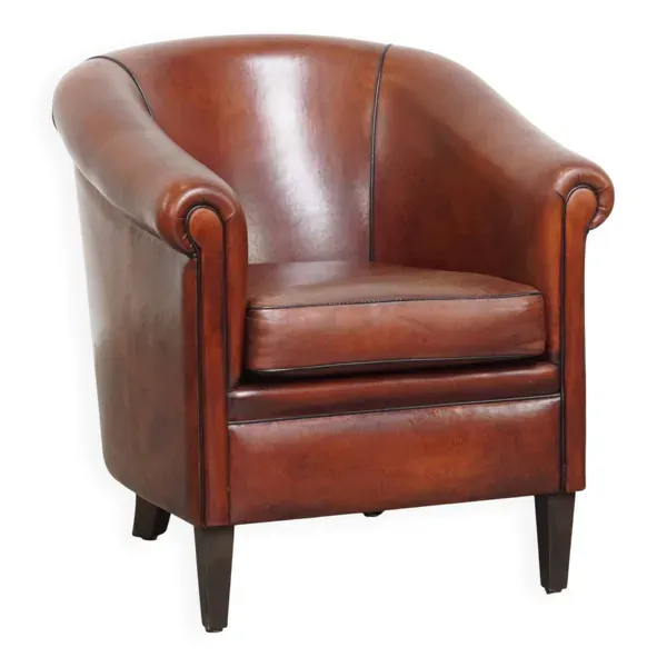 Fauteuil club en peau de mouton dans une couleur chaude et profonde, fini avec un passepoil noir.