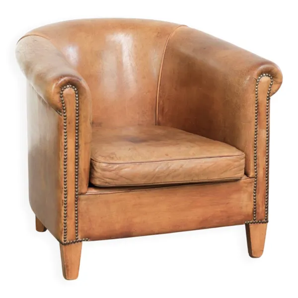 Fauteuil club en peau de mouton de couleur cognac, fini avec des clous décoratifs.