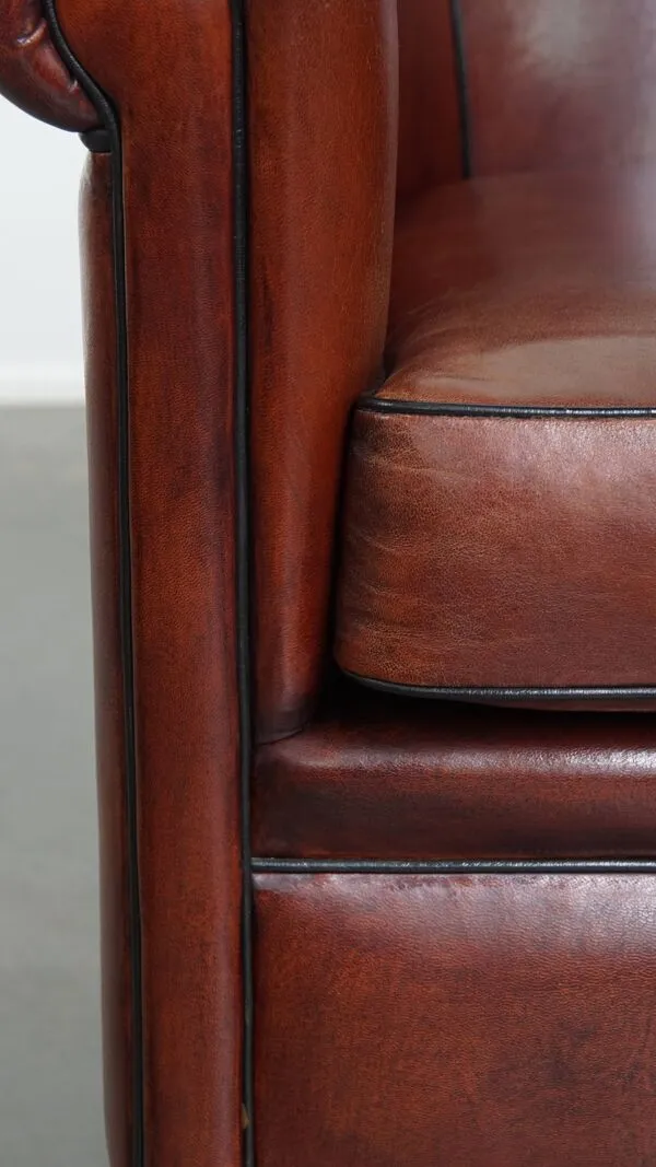 Illustration numéro 2 du produit Fauteuil club en peau de mouton dans une couleur chaude et profonde, fini avec un passepoil noir.
